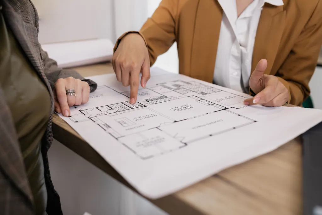 Two people pointing at a floor plan on a table